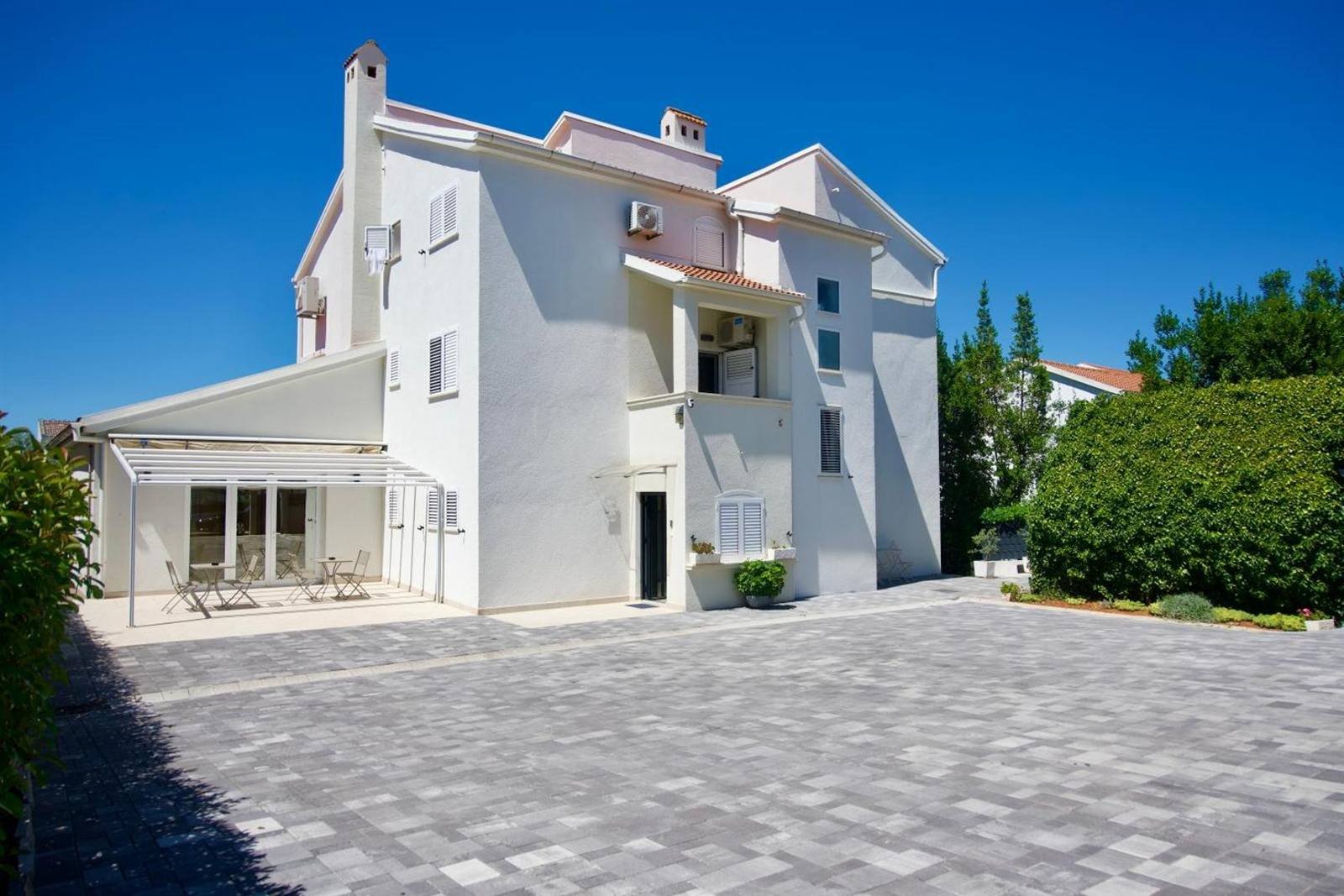 Apartments & Rooms Petra: white house with a covered terrace and a paved parking yard